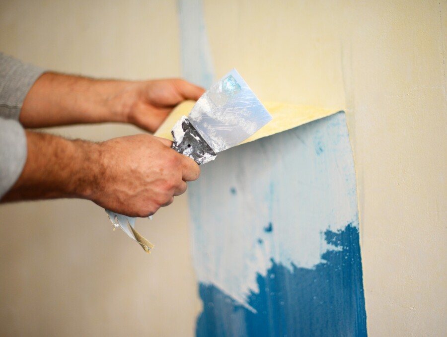 Hands peeling wallpaper from a wall during home renovation