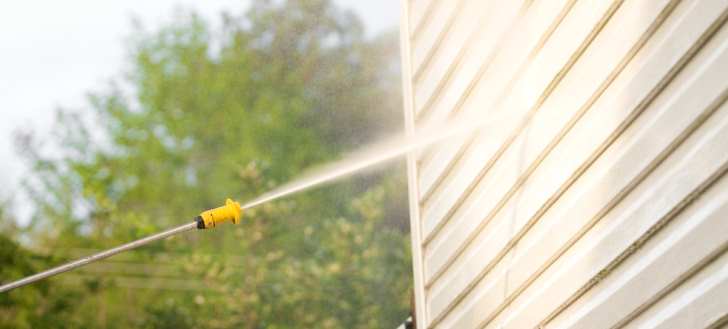 Pressure washing house siding with a spray nozzle outdoors