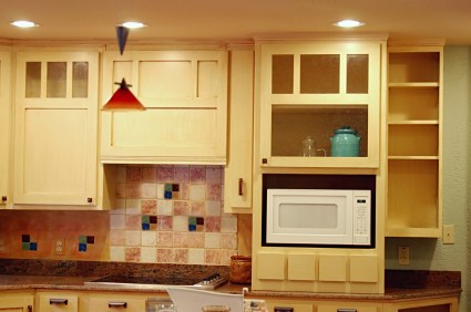 Refinished kitchen cabinets with built-in microwave, tiled backsplash, and under-cabinet lighting