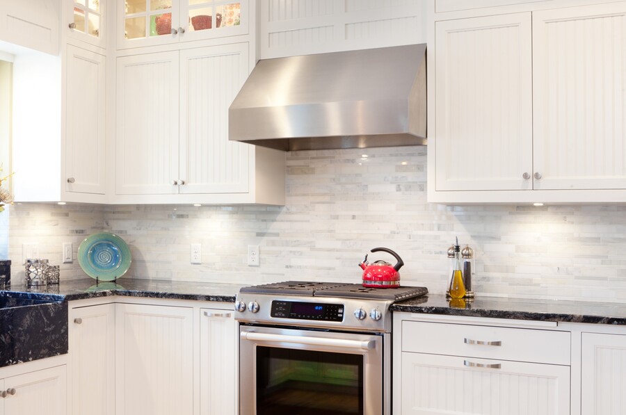 White kitchen cabinets with stainless steel range hood, stove, and dark countertop in a modern kitchen